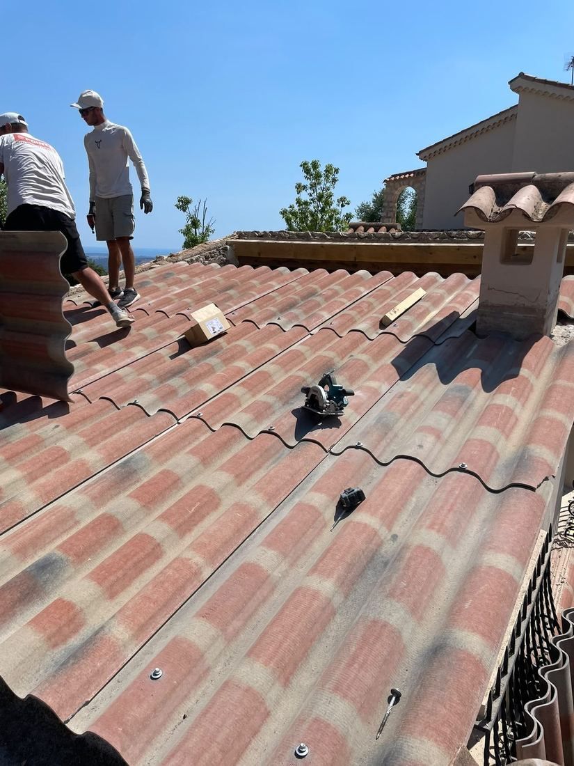 Couvreurs posant une toiture en tuiles avec vue sur un village du 06